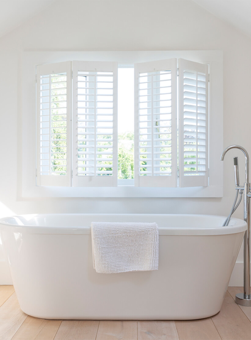 white faux wood bi-fold shutters in white bathroom with a bath